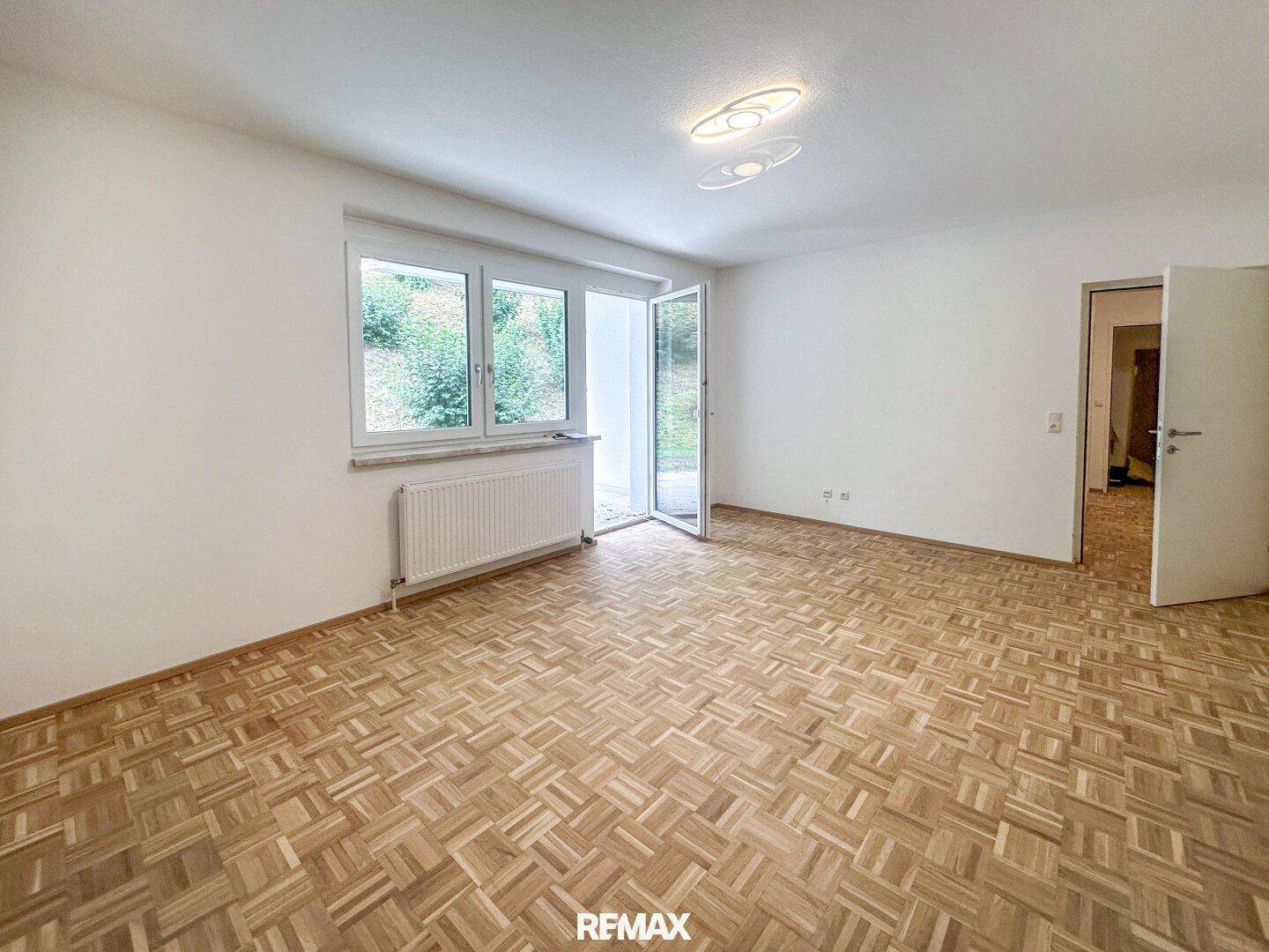 Heller Wohnraum mit Parkettboden, großen Fenstern und Zugang zu einem Außenbereich.