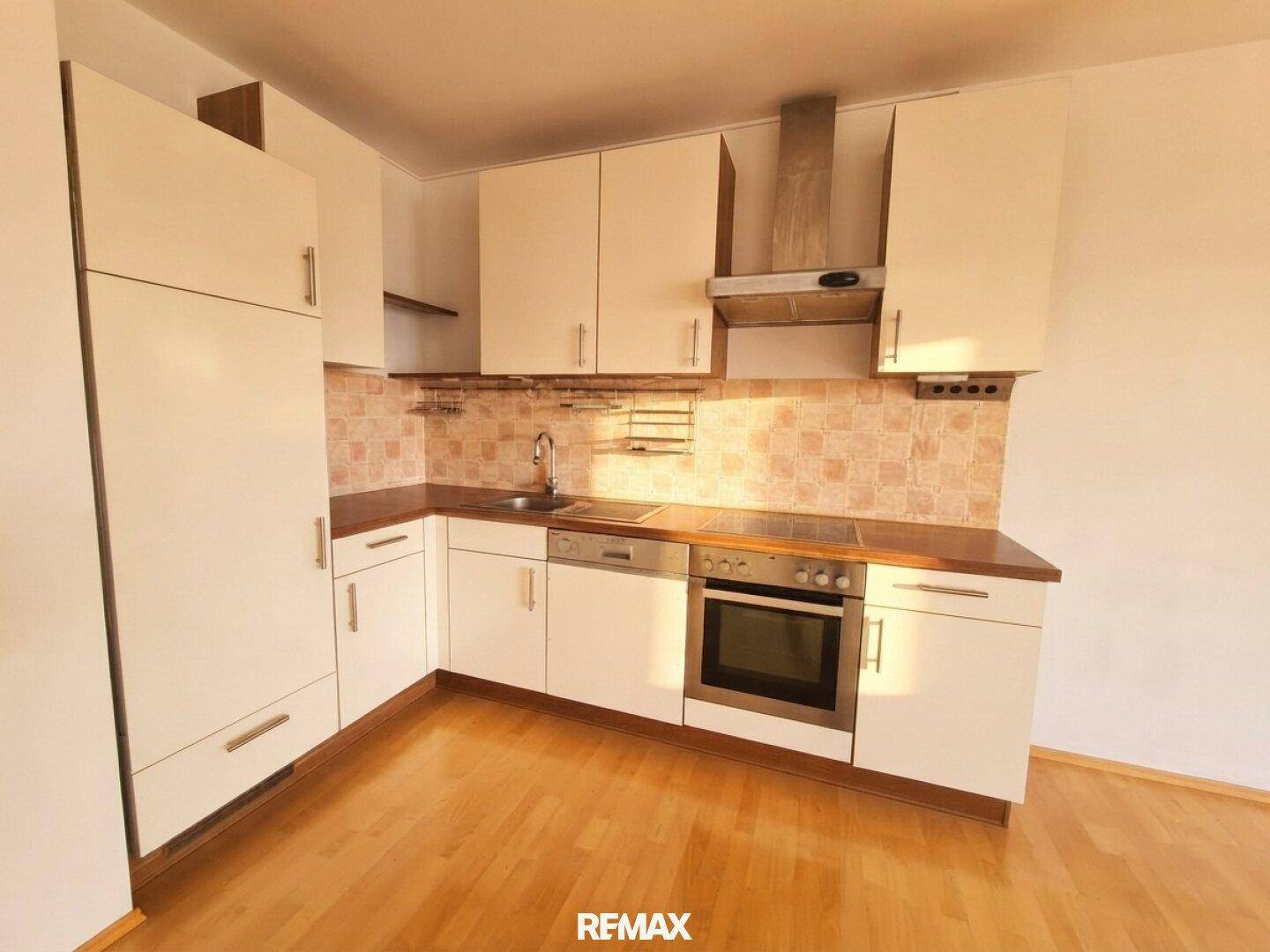 Funktionale Einbauküche mit weißen Schränken, Holz-Arbeitsplatte und integrierten Geräten.