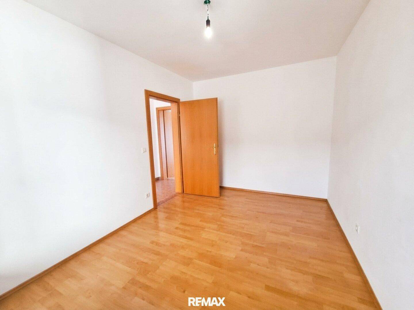 Leeres Zimmer mit hellem Parkettboden und weiß gestrichenen Wänden, ideal als Schlaf- oder Arbeitszimmer.