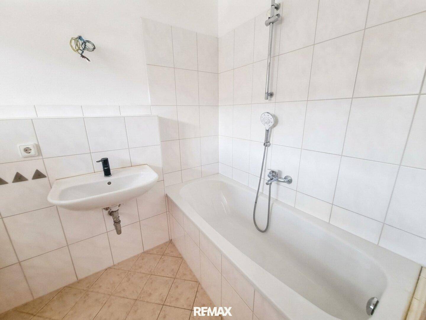 Gefliestes Badezimmer mit Badewanne, Duschfunktion und Waschbecken, in gutem Zustand.