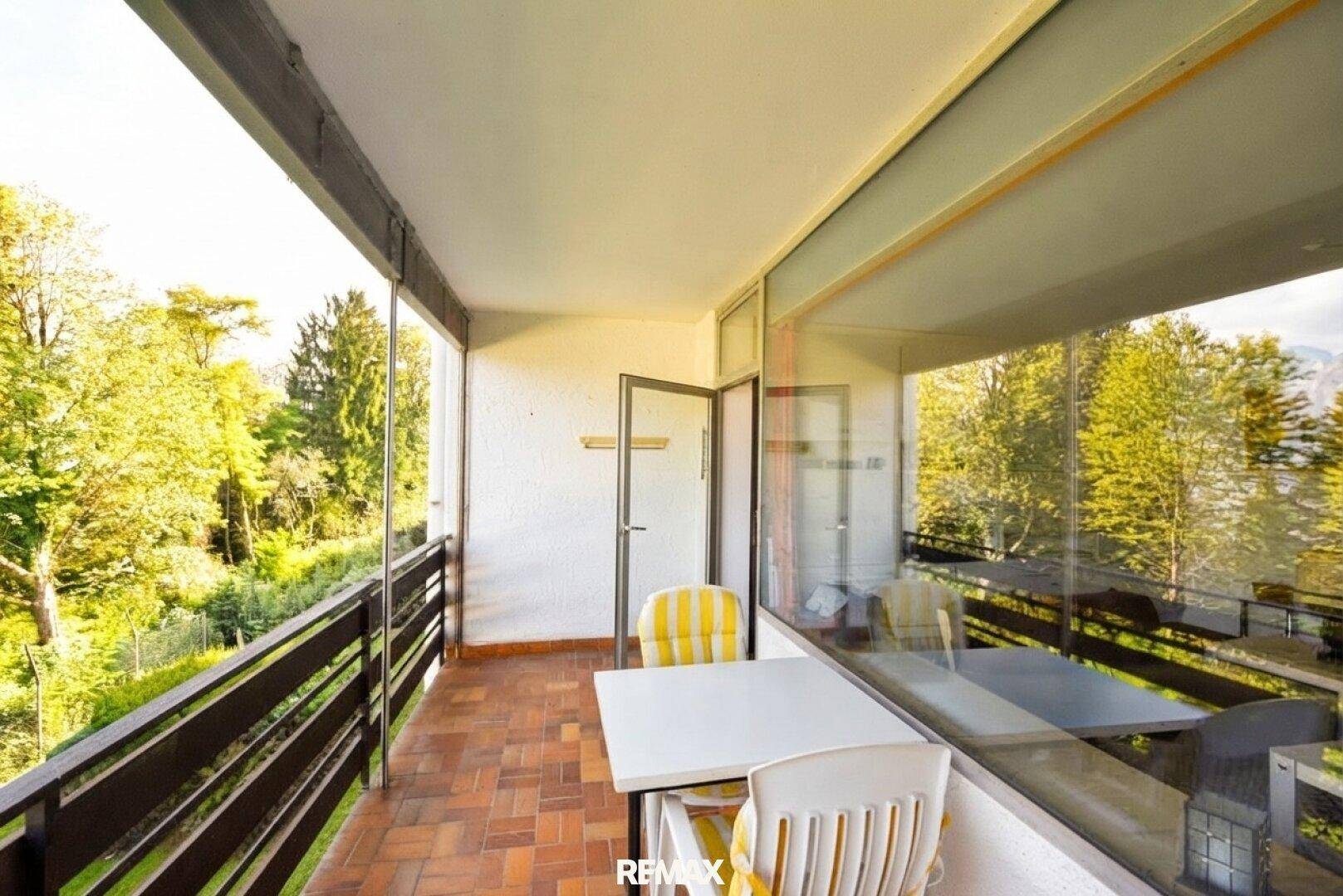 Heller Balkon mit Terrakotta-Fliesen und Sitzgelegenheiten, umgeben von viel Grün.