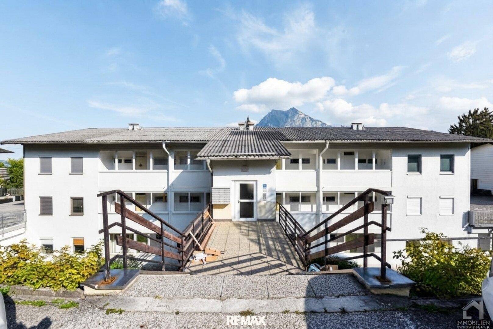 Mehrfamilienhaus mit Zugang über Rampen und Blick auf die Berge im Hintergrund.
