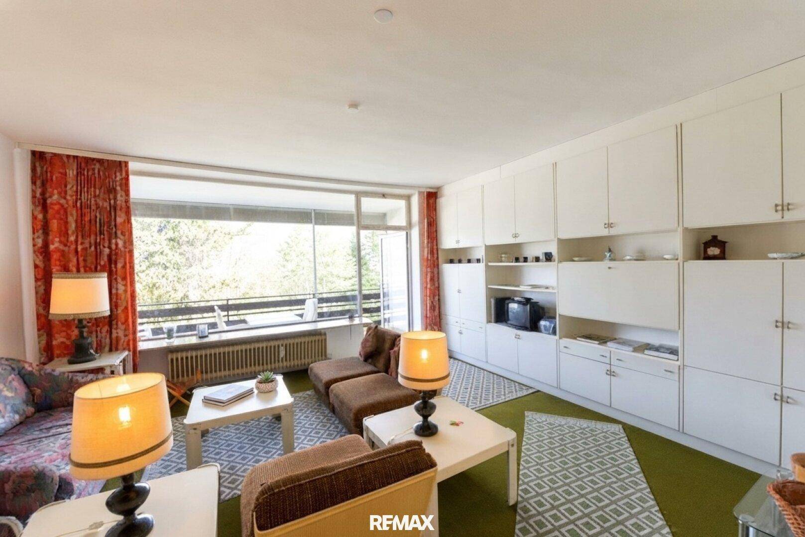 Gemütliches Wohnzimmer mit großem Fenster, Blick ins Grüne und integrierten Schränken.