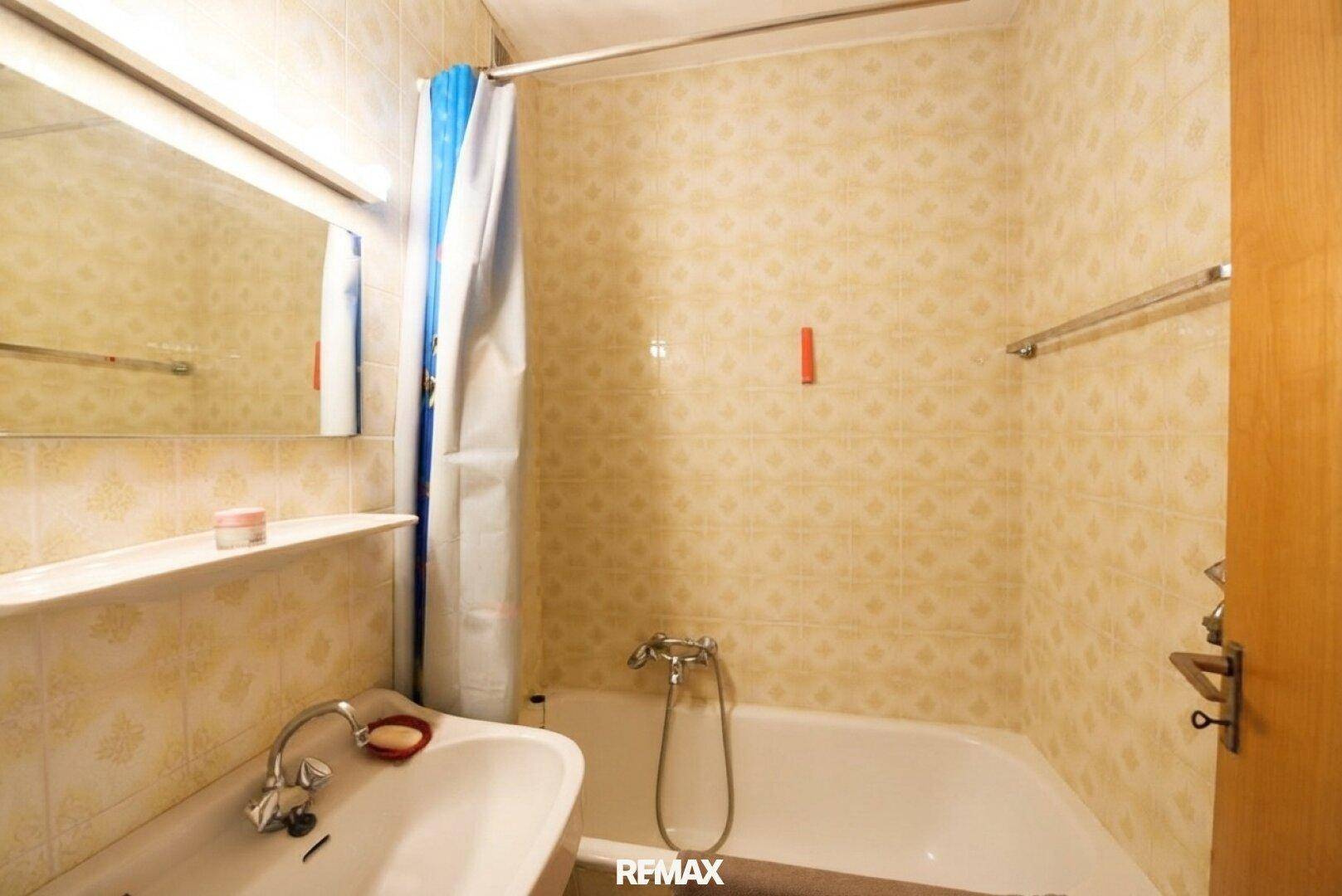 Badezimmer mit Badewanne, Duschvorhang und hellen Fliesen im Vintage-Stil.