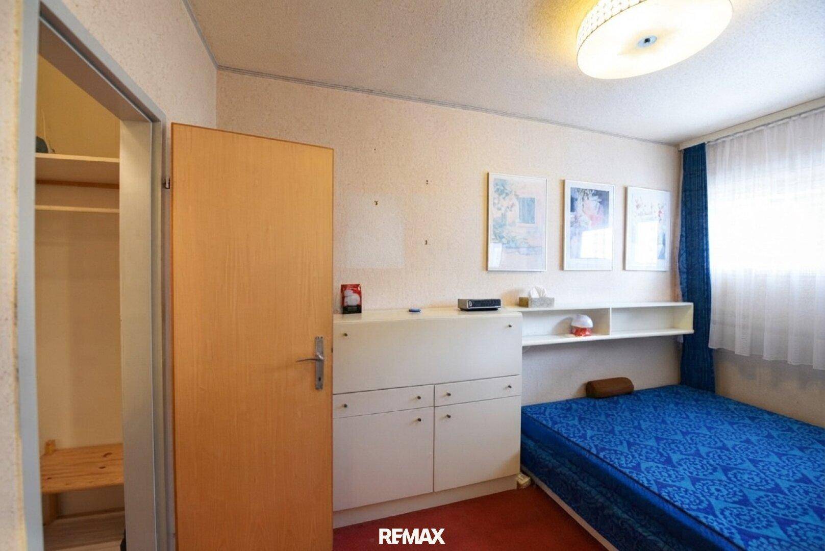 Schlafzimmer mit blauem Bett, Holzmöbeln und Zugang zu einem begehbaren Kleiderschrank.