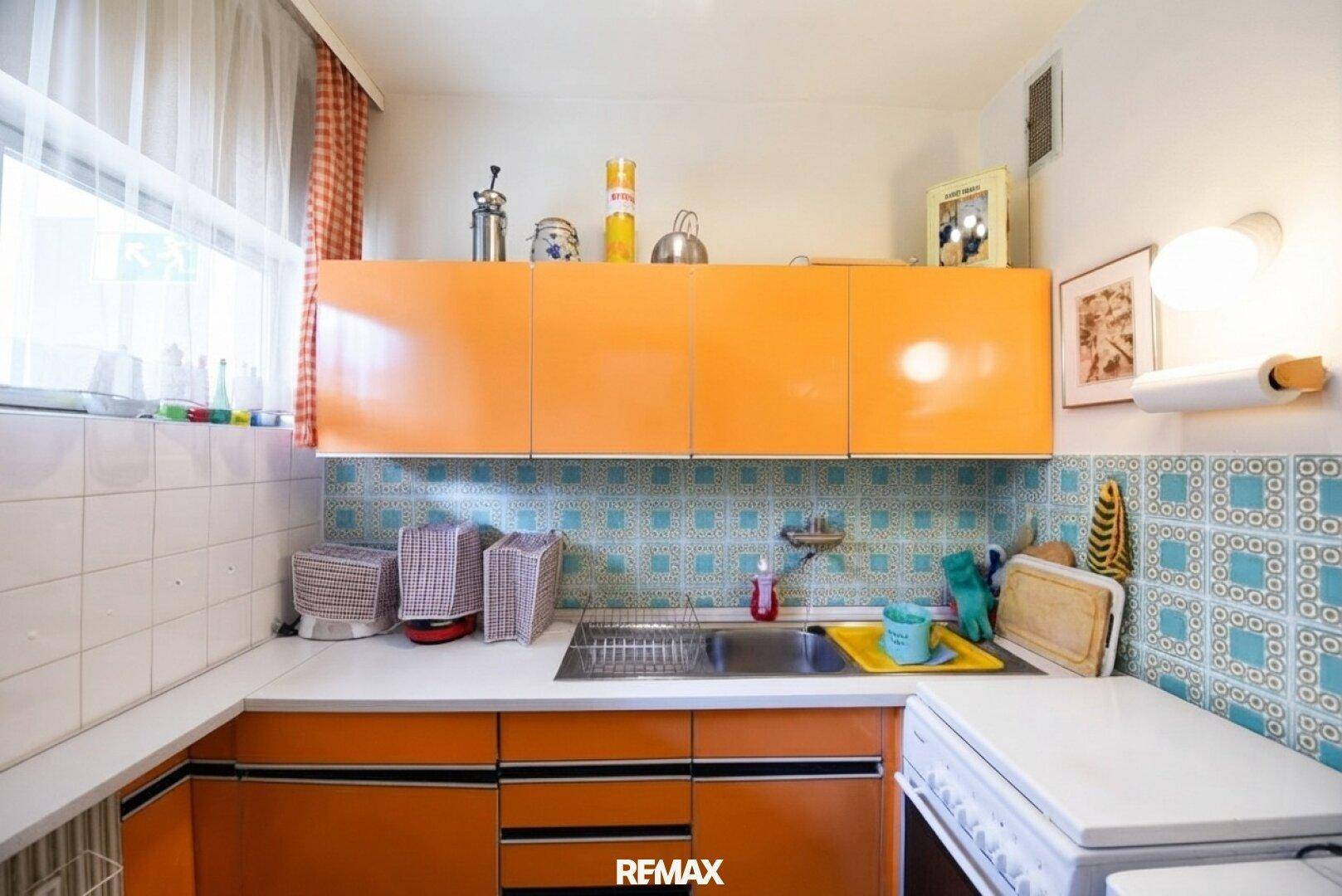 Küche im Retro-Stil mit leuchtend orangefarbenen Schränken und gemusterten Fliesen.