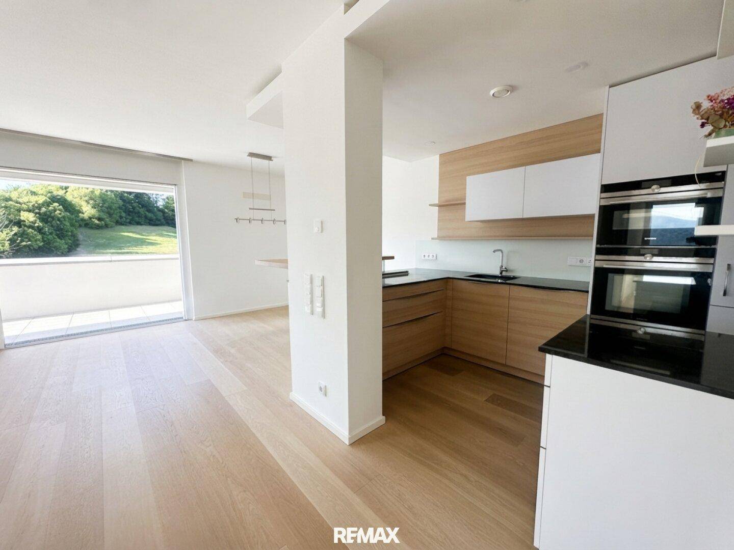 Moderne Küche mit Holzakzenten, dunkler Arbeitsplatte und Zugang zu einer Terrasse mit Grünblick.
