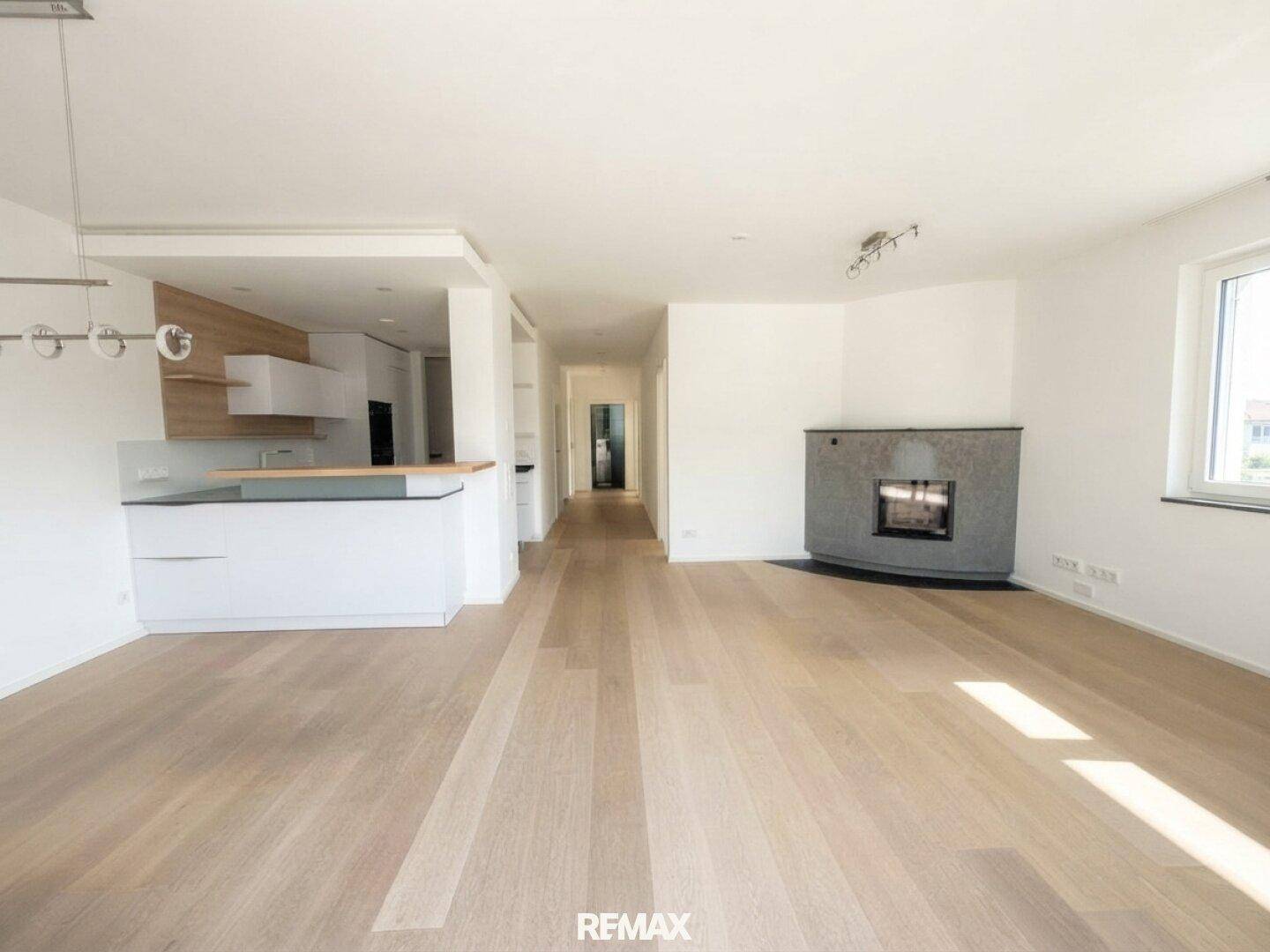 Helles, offenes Wohnzimmer mit Holzboden, Kamin und integrierter moderner Küche.