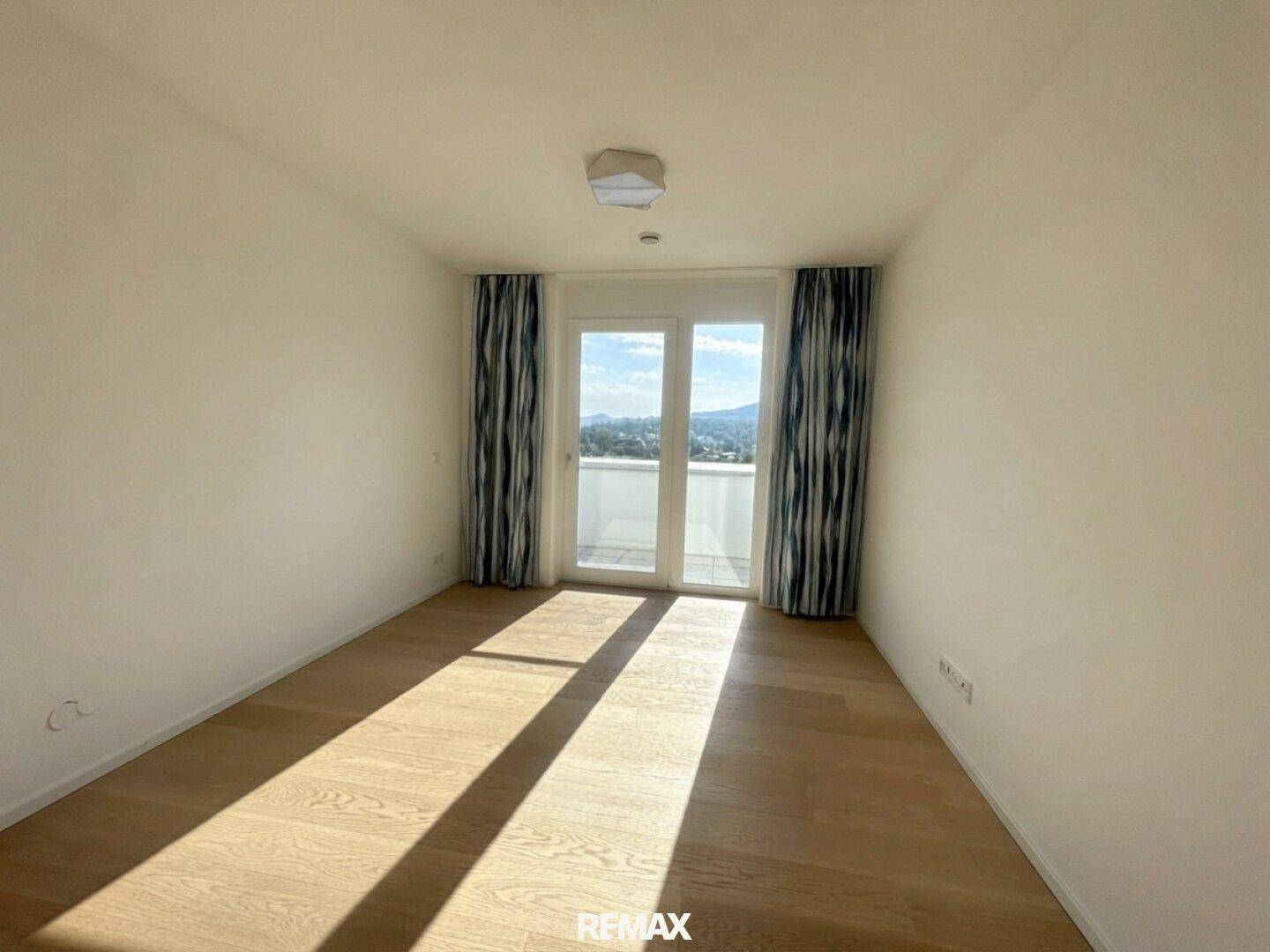 Helles Schlafzimmer mit Holzboden, großem Fenster und Balkonzugang mit Bergblick.
