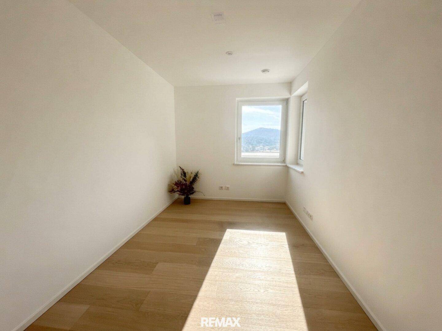 Freundliches Zimmer mit Holzboden und großem Fenster, ideal als Schlaf- oder Arbeitszimmer mit Bergblick.