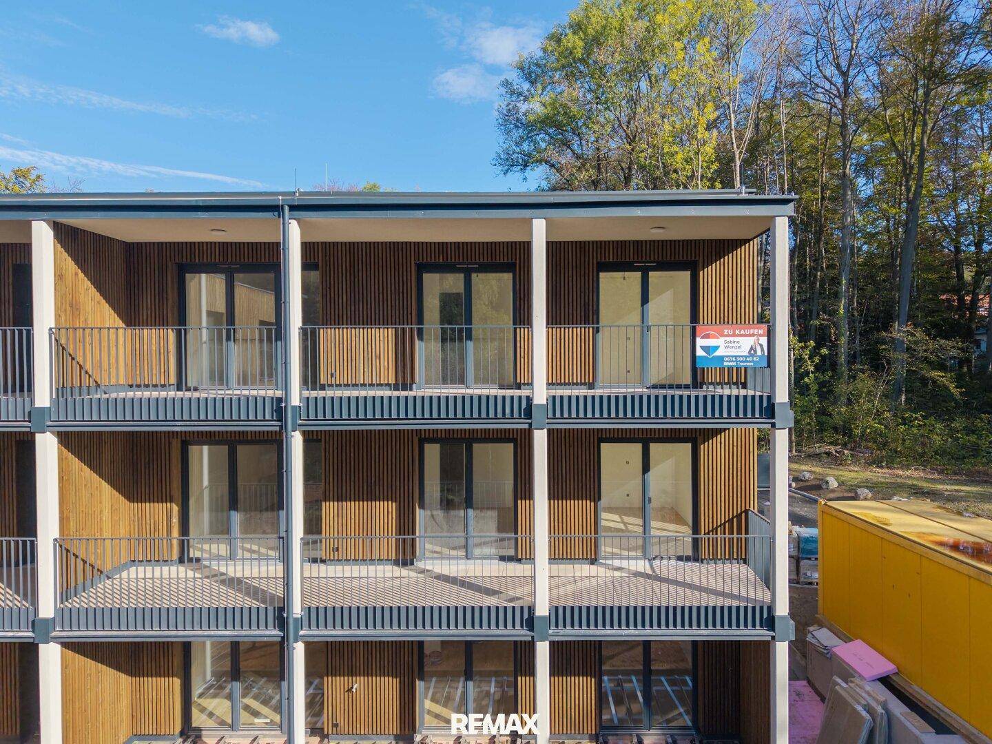 Nahaufnahme der modernen Holzfassade des Neubaus mit zahlreichen Balkonen und großen Fensterfronten.