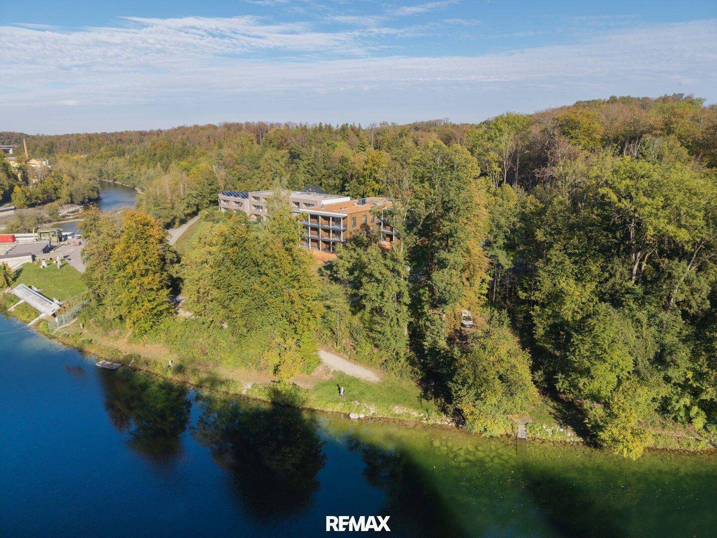 Moderne Wohnanlage am Seeufer, eingebettet in eine grüne Waldlandschaft mit Wasserblick.