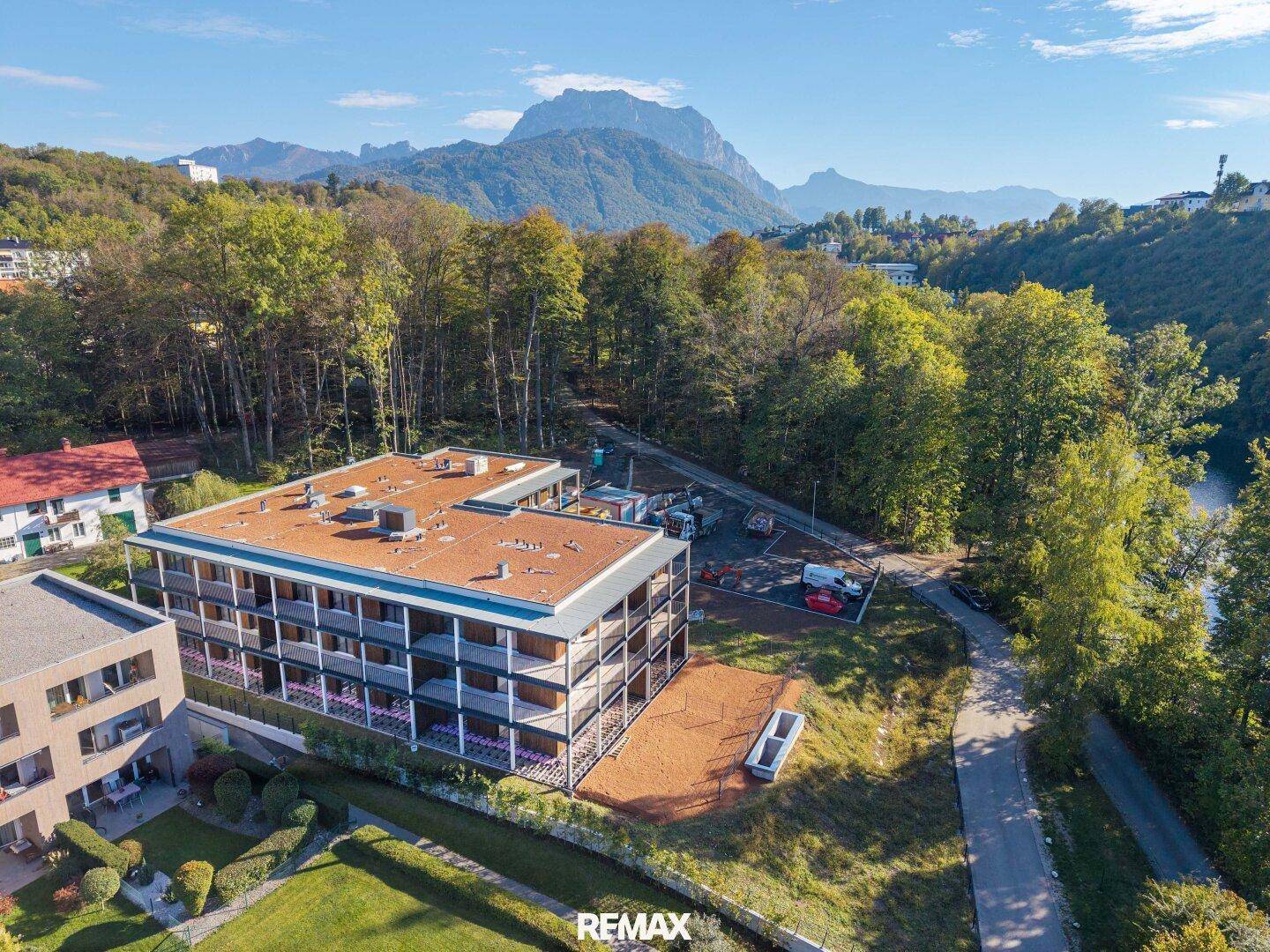 Neubau-Wohngebäude mit Flachdach und großzügigen Balkonen, umgeben von Natur und Bergen.