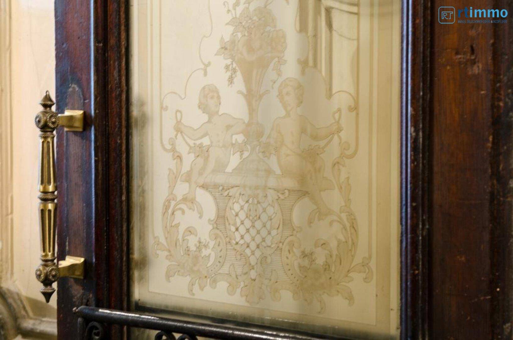 Detail einer verzierten Glastür mit geätzten Putten und einem eleganten Messinggriff.