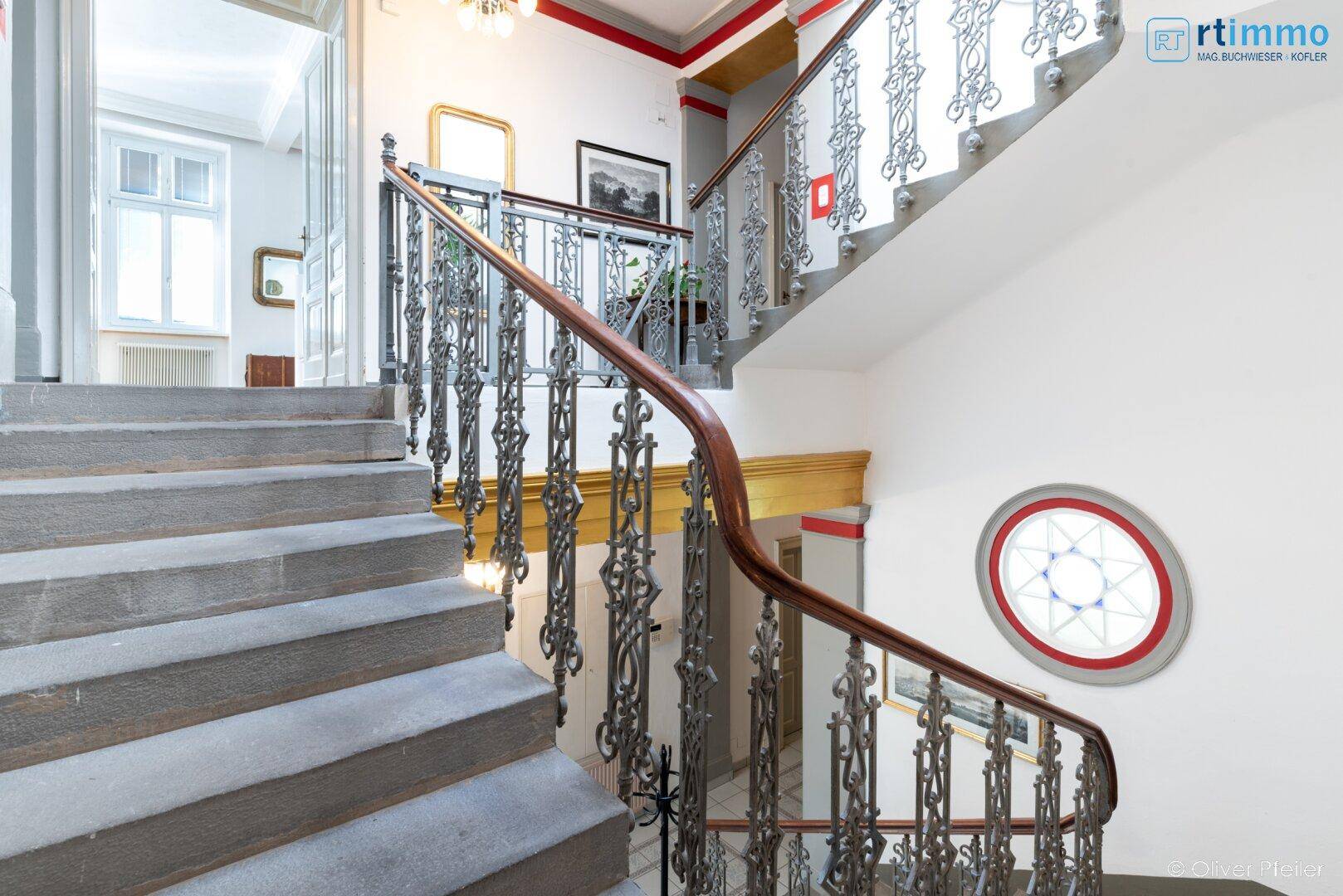 Elegante Steintreppe mit kunstvollem Geländer und hohen Decken im Treppenhaus.