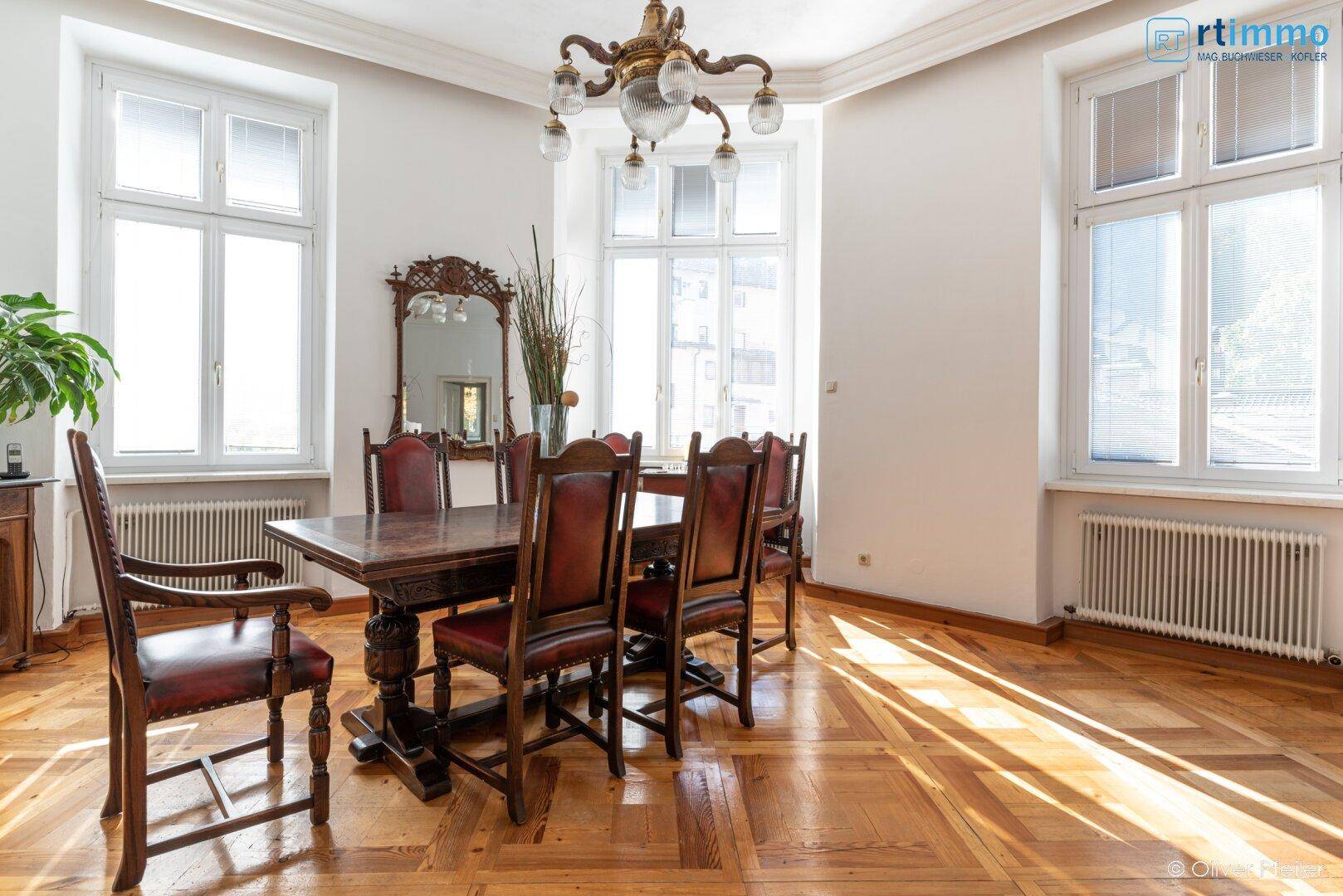 Eleganter Essbereich mit Fischgrätparkett, Kronleuchter und großen Fenstern.