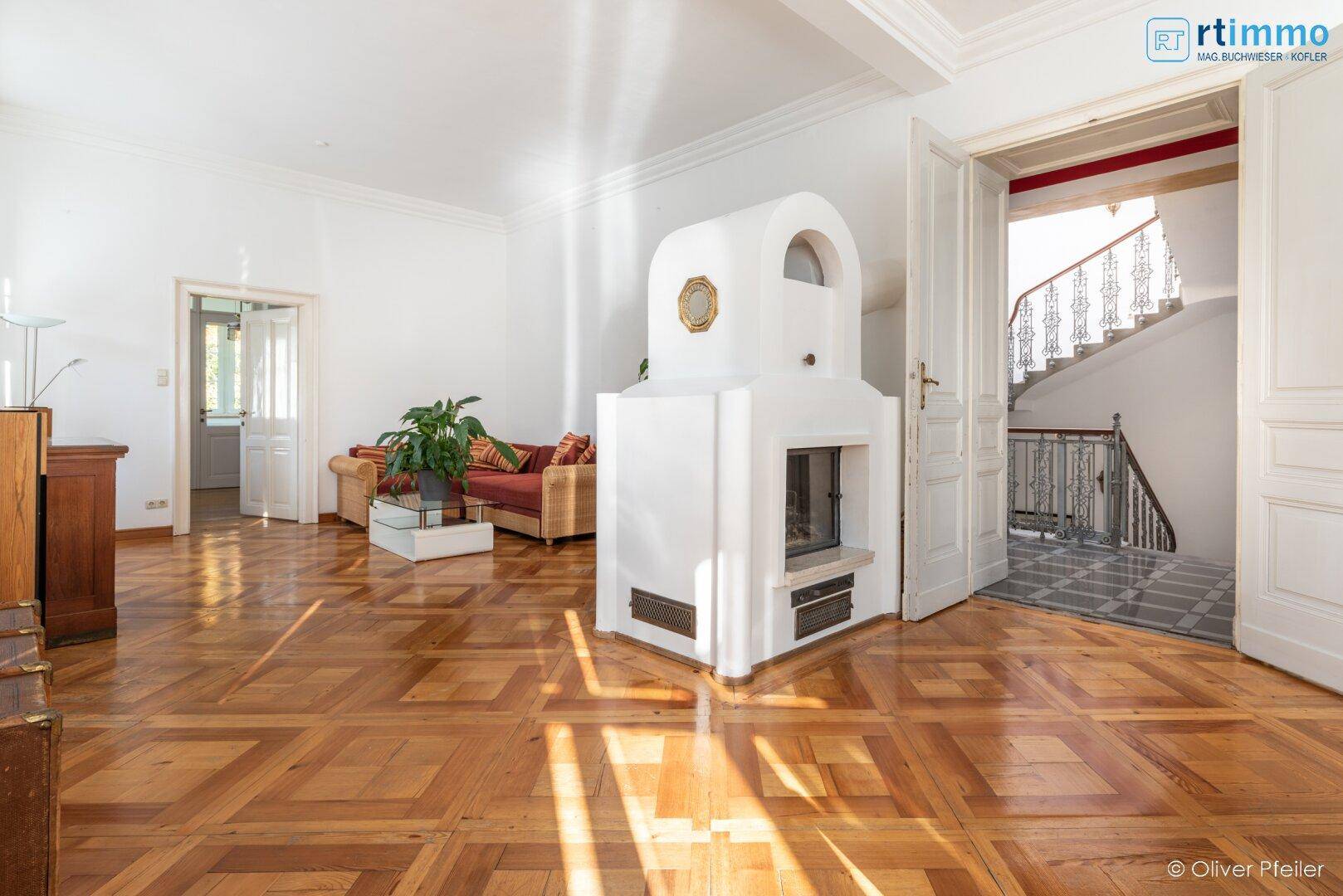 Geräumiges Wohnzimmer mit Kamin, Fischgrätparkett und Zugang zum Treppenhaus.