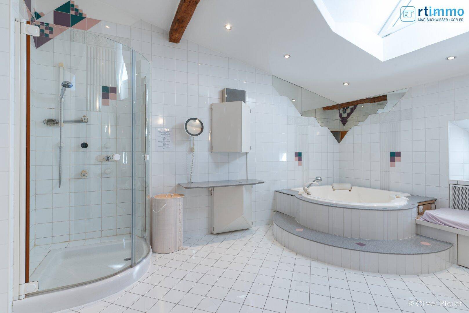 Helles Badezimmer mit weiß gefliesten Wänden, einer Duschkabine und einer eingebauten Eckbadewanne.
