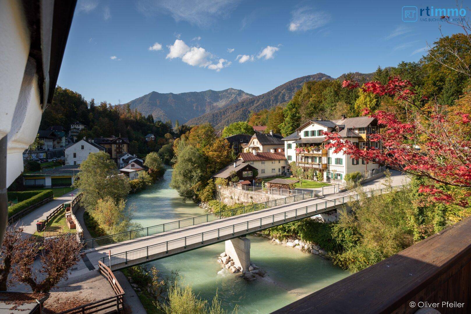 Malerischer Ausblick von einem Balkon auf einen Fluss mit Brücke, charmante Häuser und Berge.