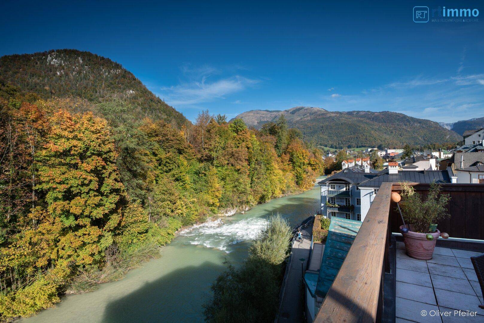 Panoramablick von einem Balkon auf einen Fluss, herbstliche Wälder und die umliegenden Berge.