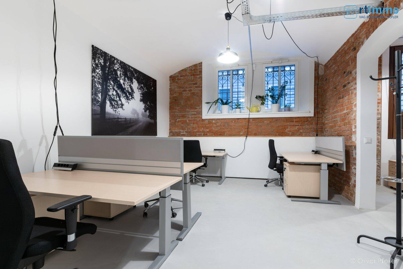 Geräumiges Büro mit mehreren Arbeitsplätzen, freiliegenden Ziegelwänden und einem großen Wandbild.