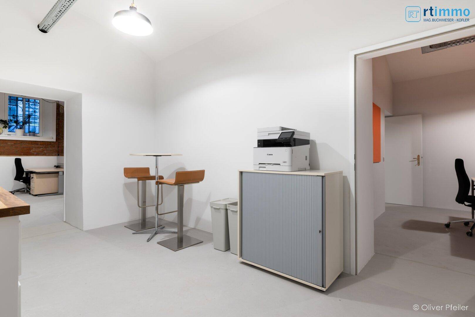 Pausenbereich mit Stehtischen und Hockern, einem Drucker und einem Rolladenschrank für Stauraum.