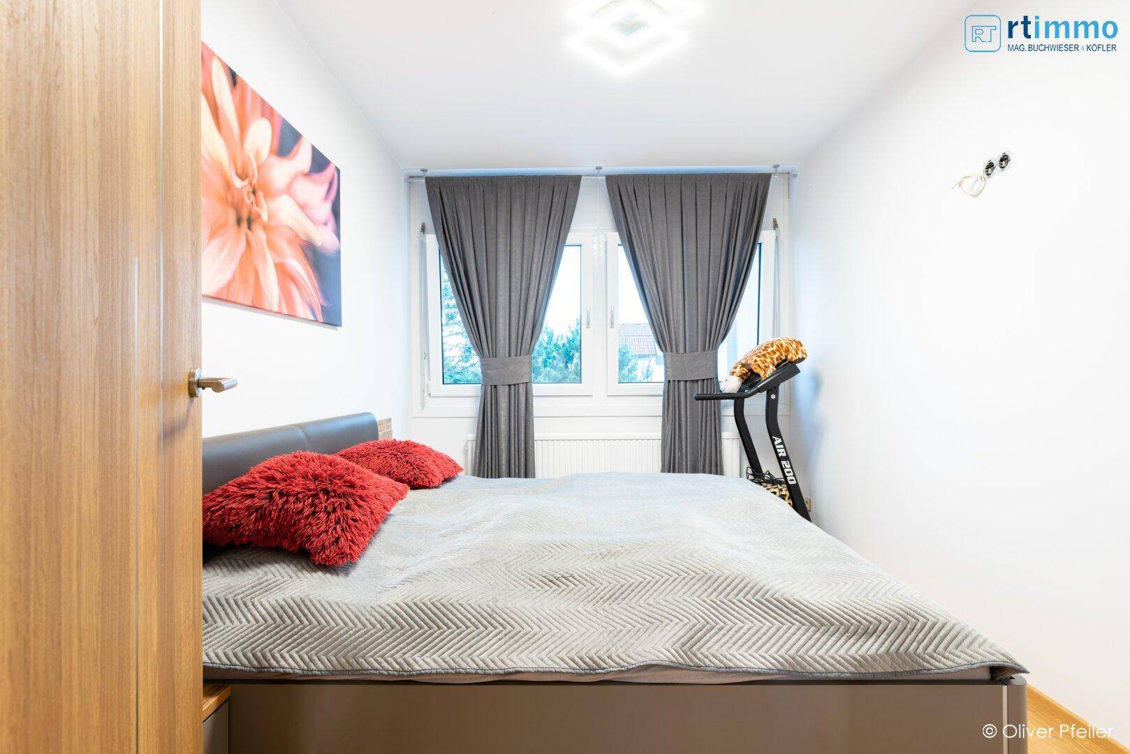 Gemütliches Schlafzimmer mit Doppelbett, grauen Vorhängen und Blick ins Grüne durch die Fenster.
