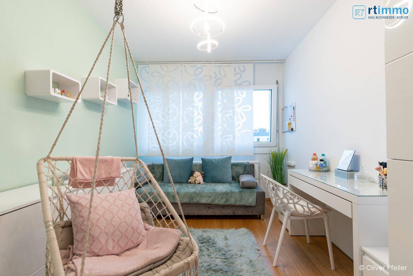 Helles Kinderzimmer mit Schaukelstuhl, Sofa und Schreibtisch, ideal für Spiel und Lernen.