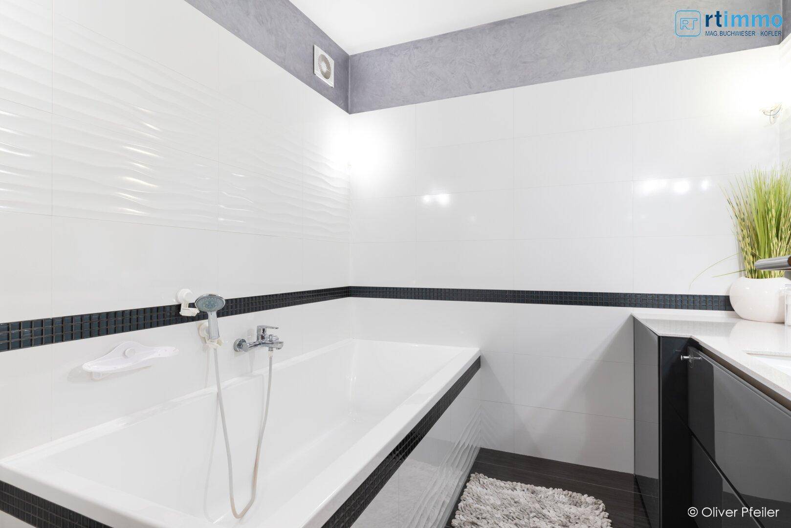 Modernes Badezimmer mit Badewanne, weißen Wandfliesen und dunklem Akzentstreifen.