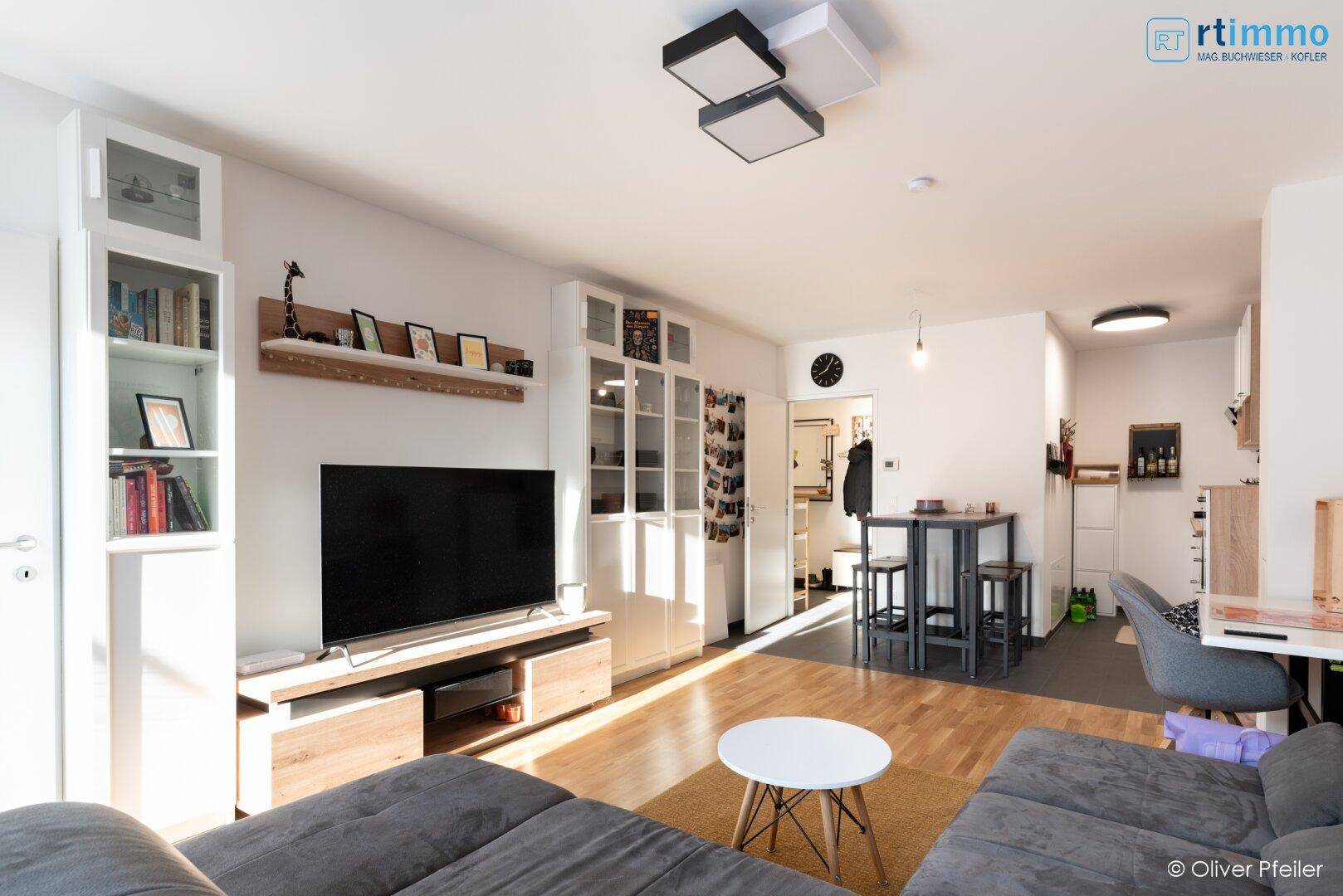 Heller Wohnbereich mit Sofa, Fernseher und Essplatz, durchflutet von natürlichem Licht.