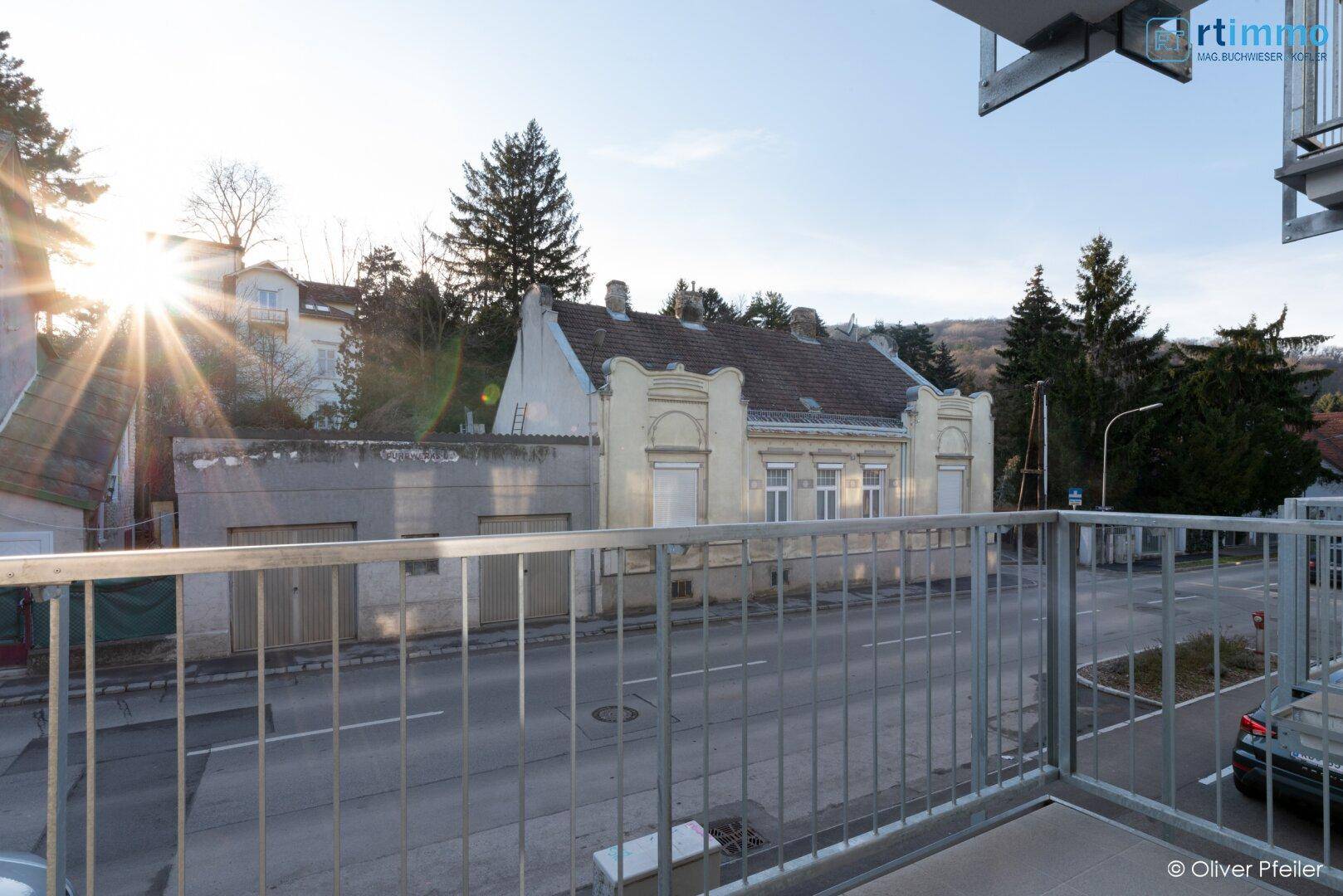 Balkon mit Blick auf die Straße und gegenüberliegende Gebäude, sonniger Nachmittag.