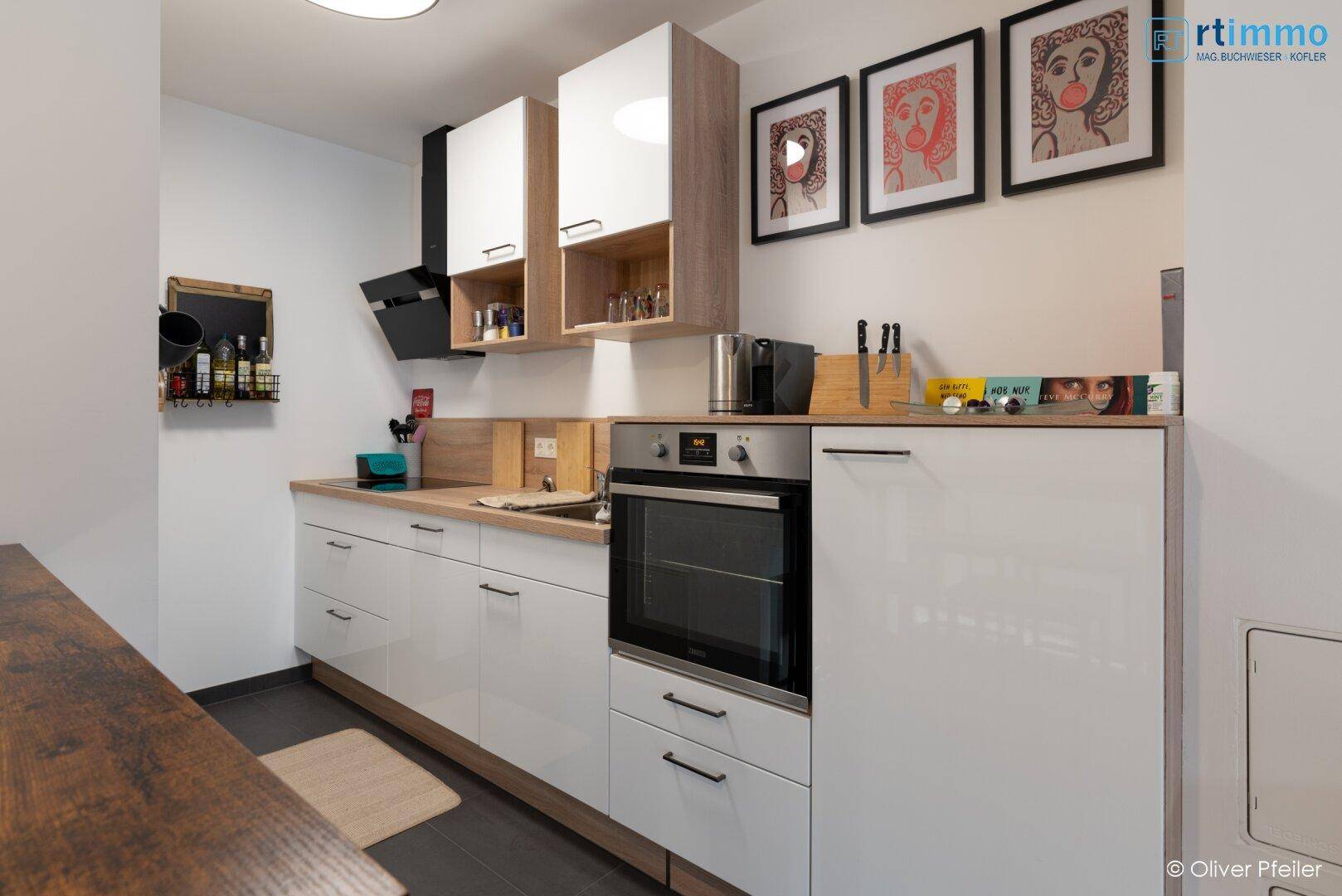 Moderne Einbauküche mit weißen Hochglanzfronten, integriertem Backofen und Dunstabzugshaube.