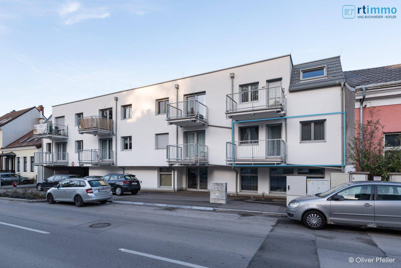 Moderne Wohnhausfassade mit mehreren Balkonen und großen Fenstern an einer Straße gelegen.