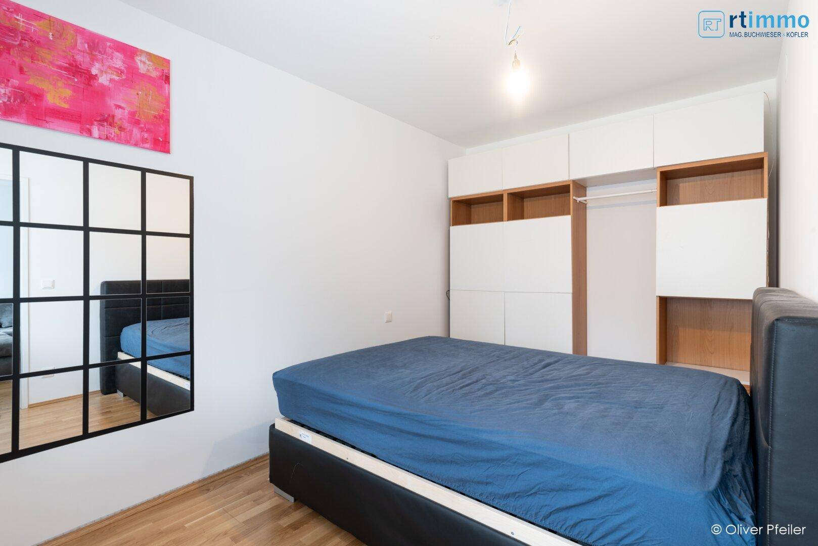 Schlafzimmer mit Doppelbett, Einbauschrank und Holzfußboden, hell und funktional eingerichtet.