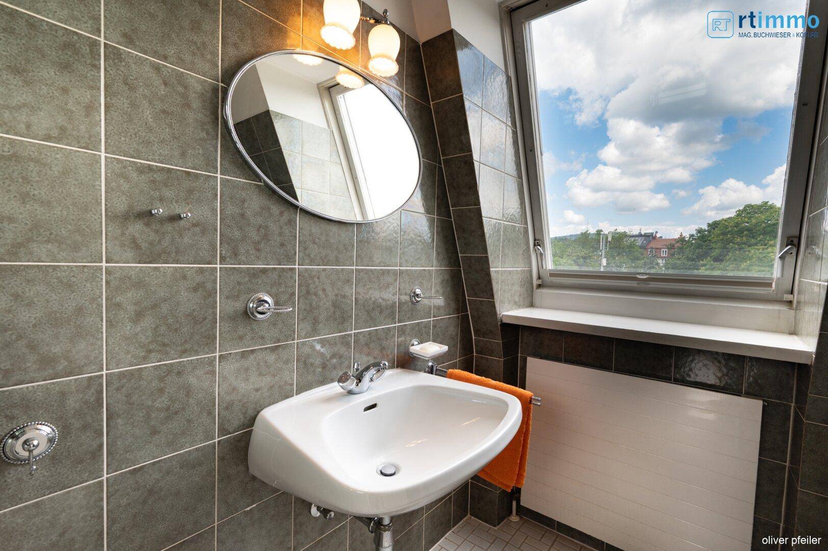Badezimmer mit Waschbecken, Spiegel und Fenster für Tageslicht.