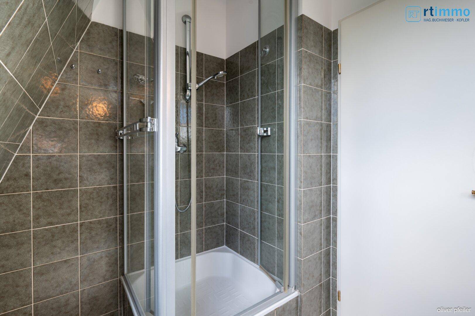Badezimmer mit Duschkabine und grauen Fliesen an Wänden und Boden.