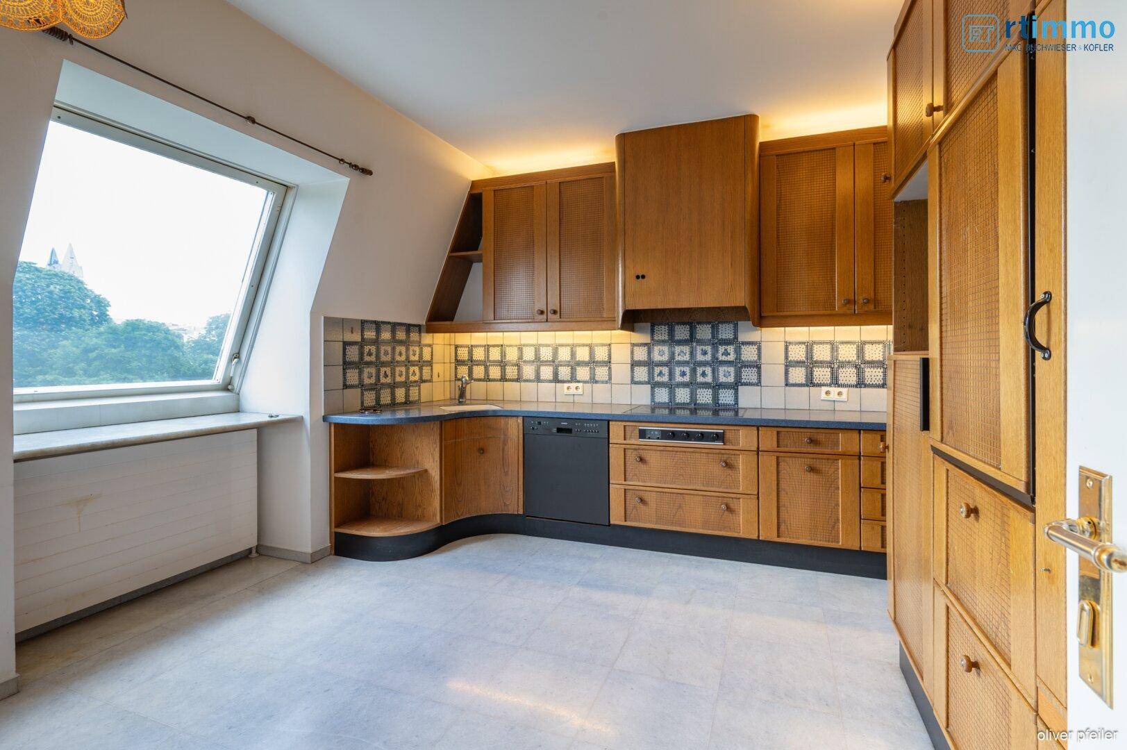 Funktionale Küche mit Holzschränken, Fliesenboden und Dachfenster.