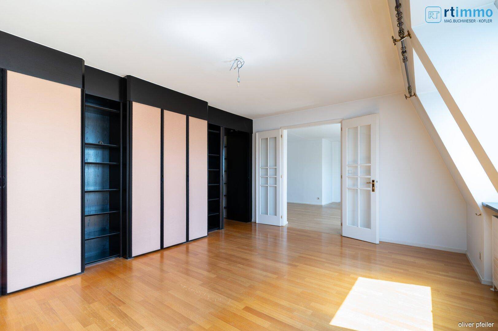 Geräumiges Zimmer mit Einbauschränken, Parkettboden und Zugang zu weiteren Räumen.
