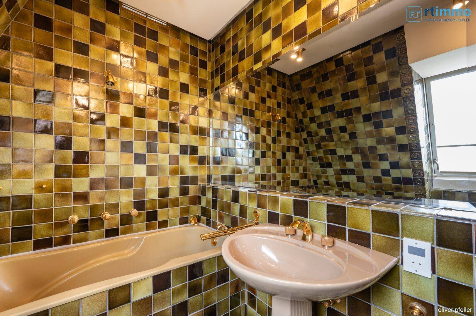 Badezimmer mit Badewanne, Waschbecken und auffälligen braun-gelben Fliesen.