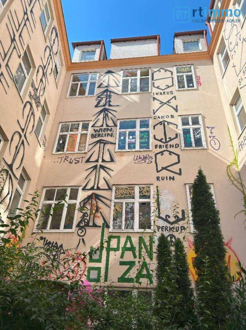 Innenhoffassade eines Altbaus mit zahlreichen Fenstern und auffälligen Graffiti, die eine Renovierung benötigen.