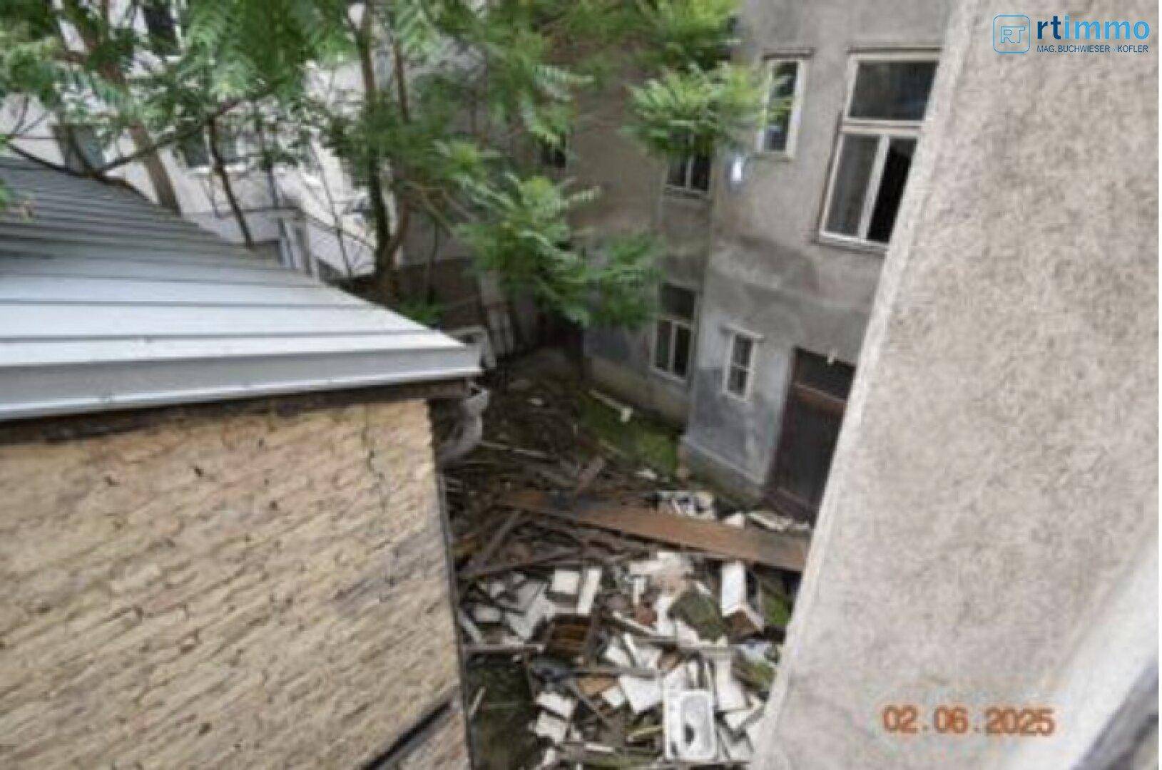 Blick in einen verwilderten Innenhof mit Bauschutt und Bäumen, der eine Sanierung benötigt.