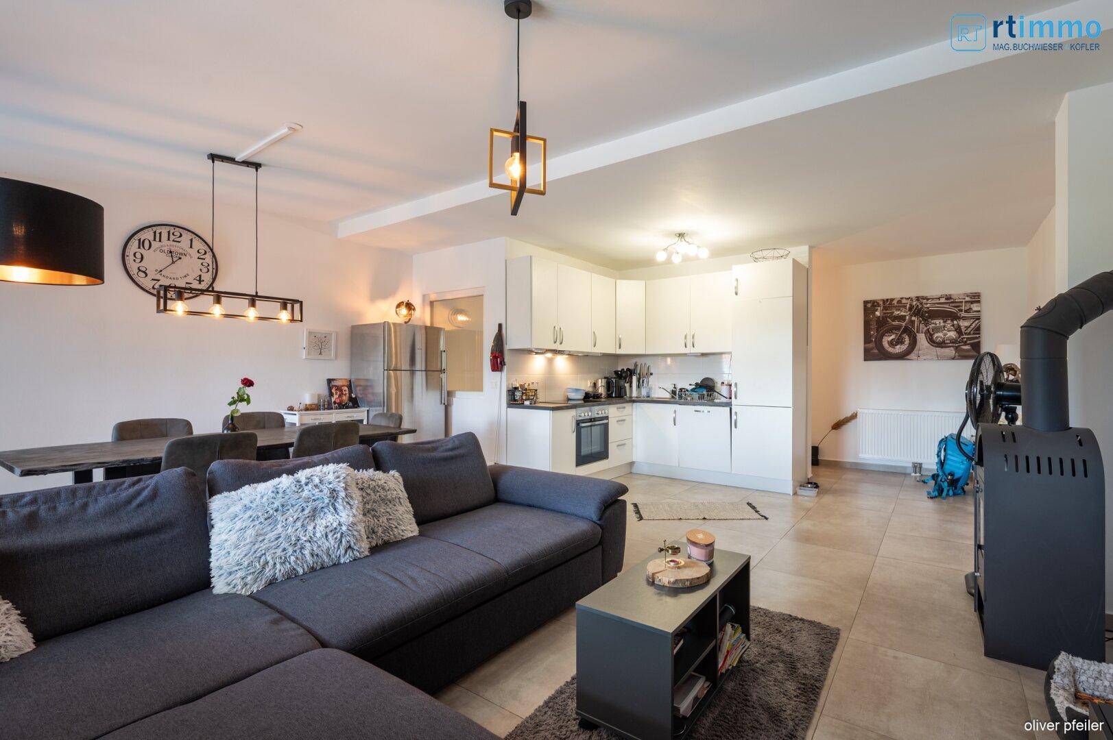 Geräumiger Wohnbereich mit integrierter weißer Küche, gemütlichem Sofa und Holzofen.