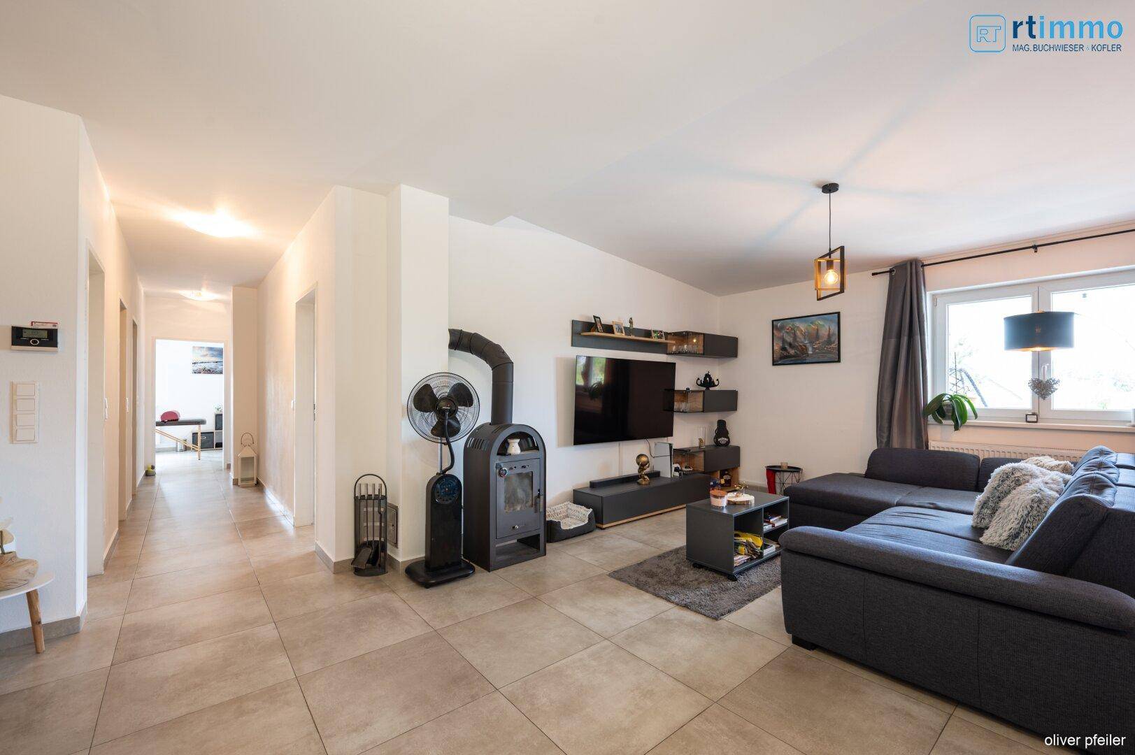 Gemütliches Wohnzimmer mit modernem Holzofen, großem Sofa und Zugang zum Flur.