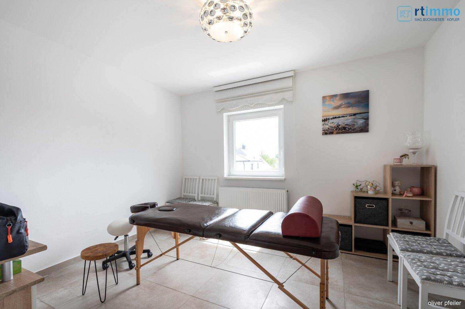 Helles Zimmer, eingerichtet als Therapieraum oder Büro, mit Fenster und Fliesenboden.