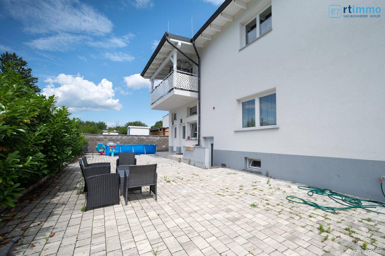 Gepflasterter Außenbereich neben dem Haus mit einem Aufstellpool und Sitzgelegenheiten.