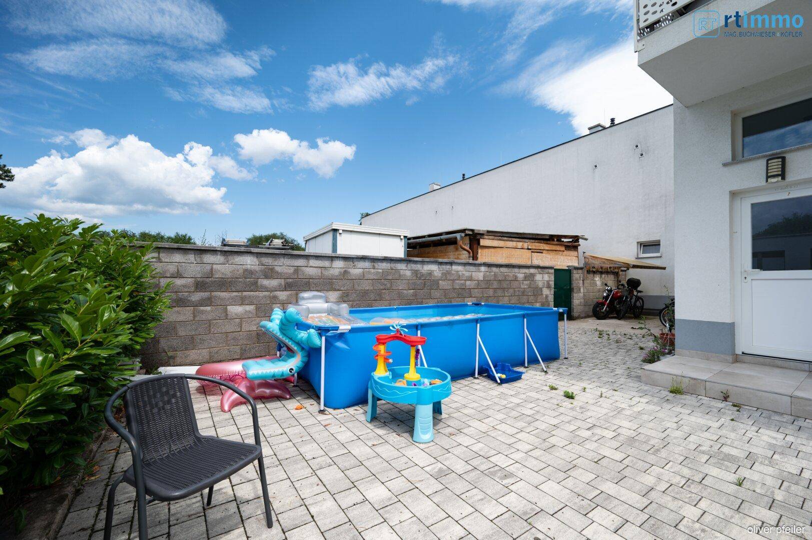 Detailansicht des gepflasterten Bereichs mit blauem Aufstellpool und einem Stuhl.
