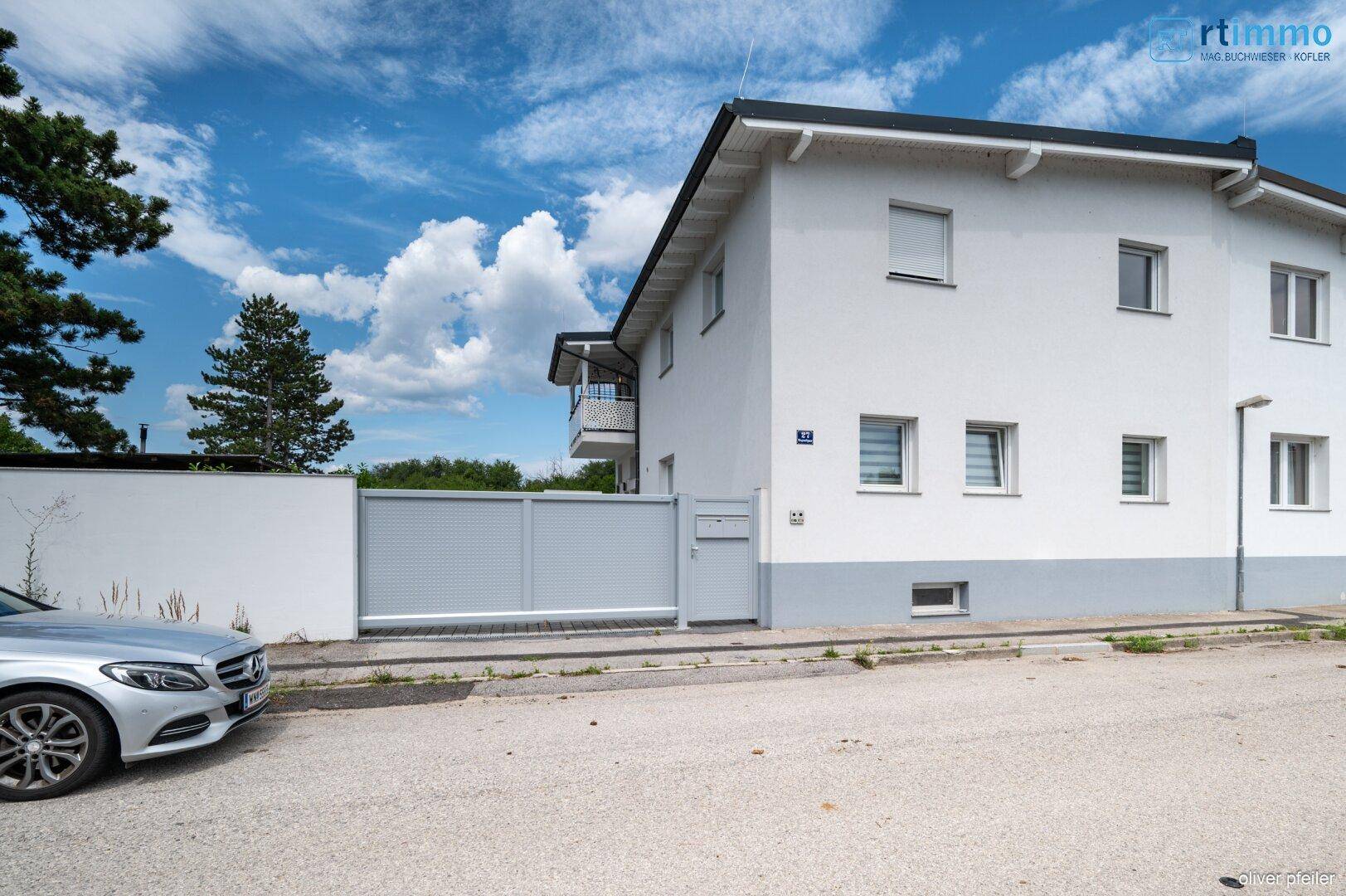 Ansicht des Hauses von der Straße mit geparktem Auto und modernem Eingangstor.