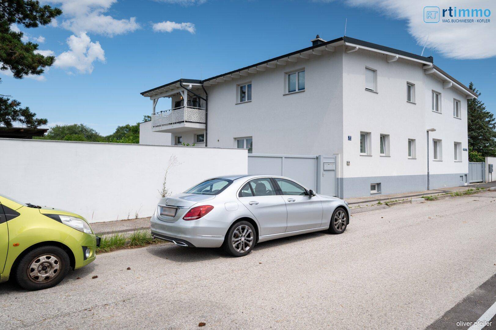 Straßenansicht des Wohnhauses mit einem silbernen Auto davor und weißer Fassade.