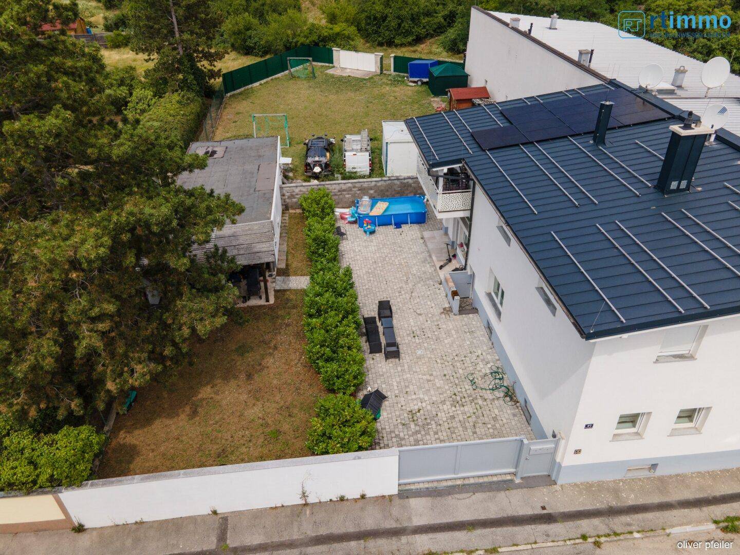 Luftaufnahme des Hauses mit gepflastertem Hof, Pool und einer Reihe junger Bäume.