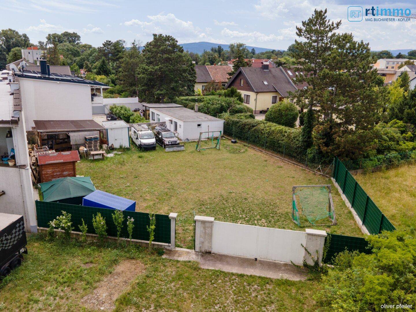 Luftaufnahme des Grundstücks mit Garten, Nebengebäuden und Blick auf die umliegende Wohngegend und Berge.